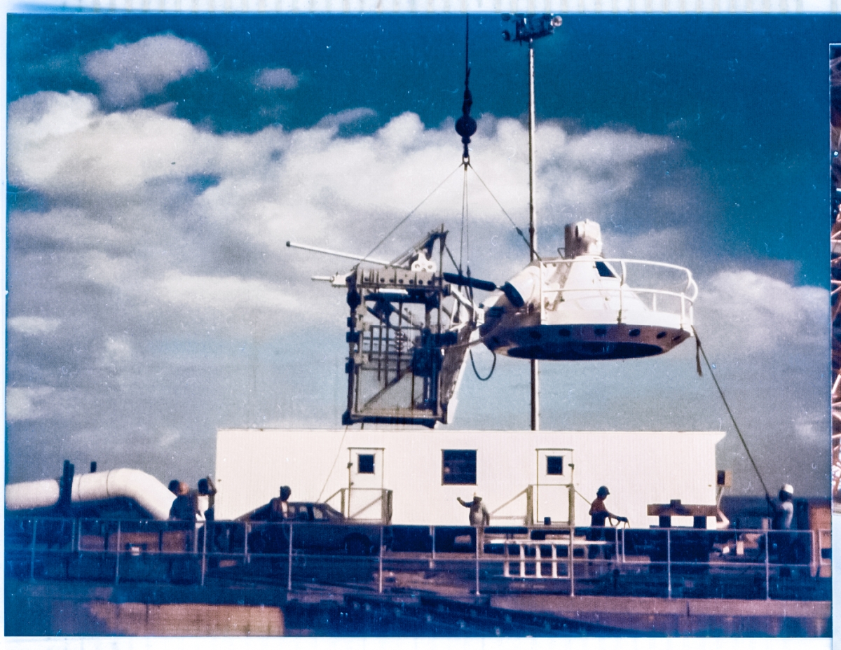 At Space Shuttle Launch Complex 39-B, Kennedy Space Center, Florida, The Gaseous Oxygen Vent Hood, informally referred to as the “Beanie Cap” is lifted off of its support cribbing in front of Boeing’s TTV trailer on the east side of the Flame Trench, from where it will then be lifted into place and  attached to the end of the Gox Arm Main Truss which has already been installed near the top of the Fixed Service Structure.